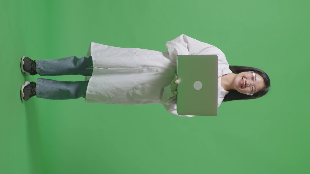 cuerpo lleno de mujer científica asiática sonriendo a la cámara mientras está de pie y trabajando en una computadora portátil en el laboratorio de fondo de la pantalla verde