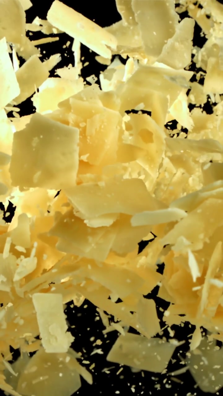 Parmesan Cheese Flakes Falling in Slow Motion on Black Background