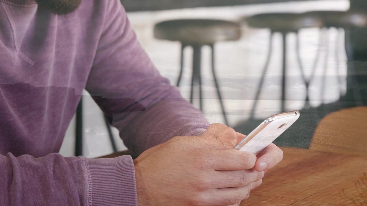 Bearded man looking down and tapping phone, with animated charts appearing over hands for tech