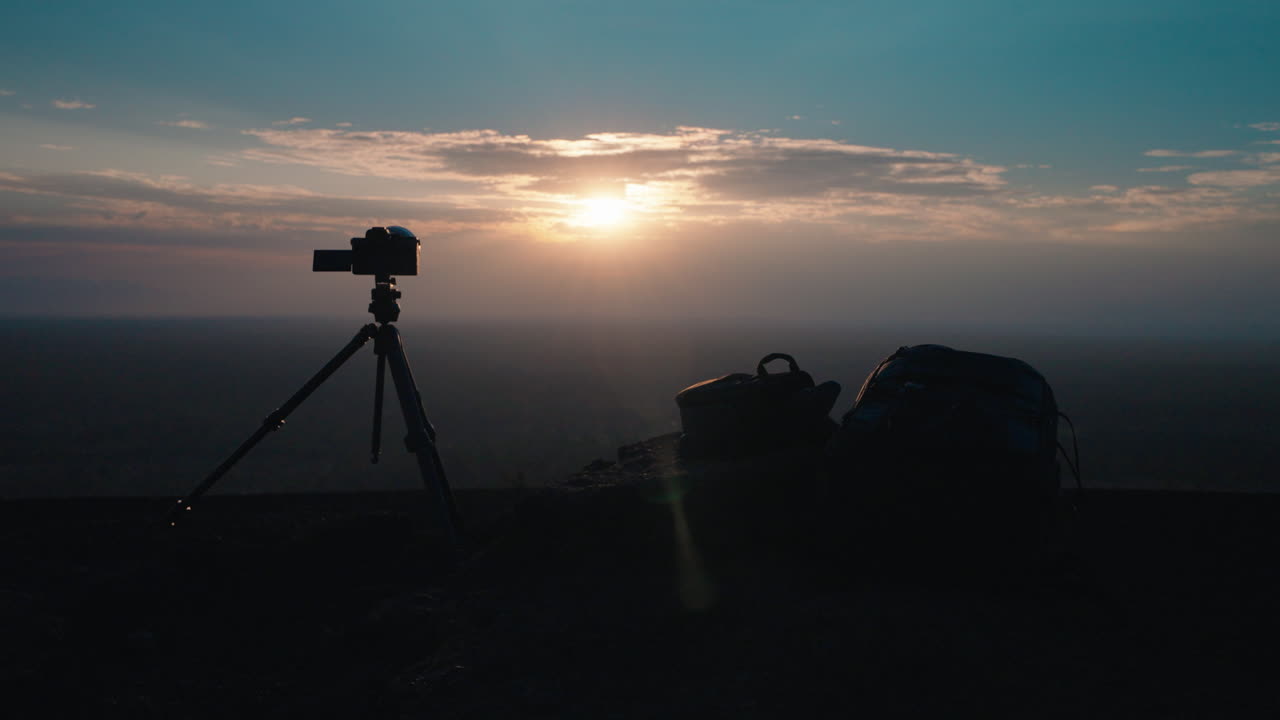 Camera and Backpacks Silhouetted Against a Scenic Sunset