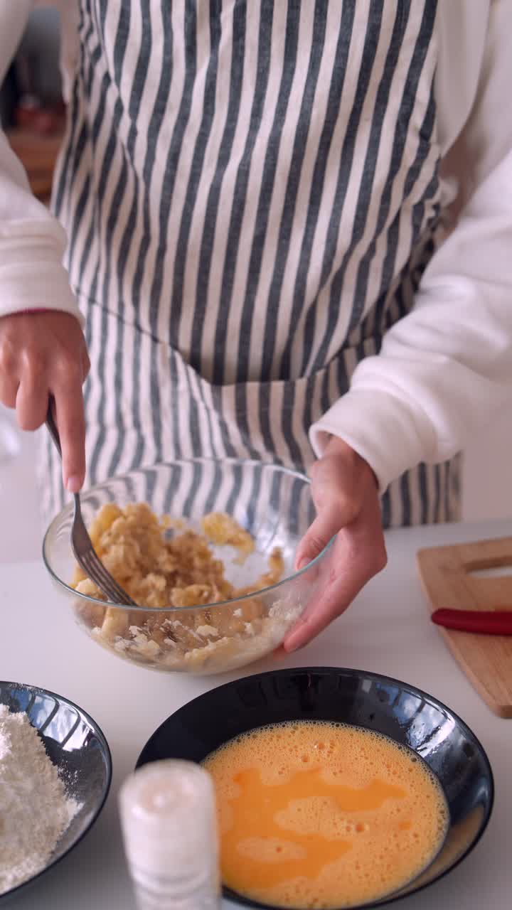 Mani che schiacciano banane con una forchetta in una ciotola di vetro