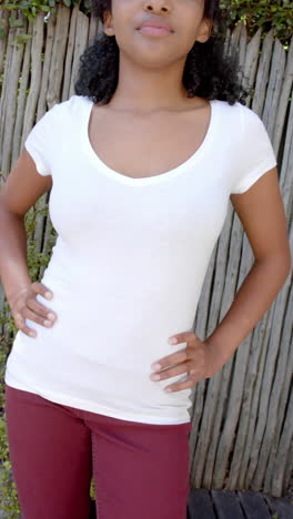 vertical video of biracial woman in white t shirt with hands on hips outdoors, slow motion