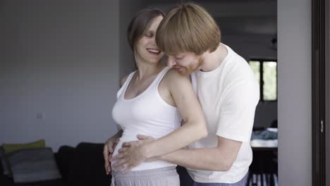 smiling husband walking and hugging his pregnant wife