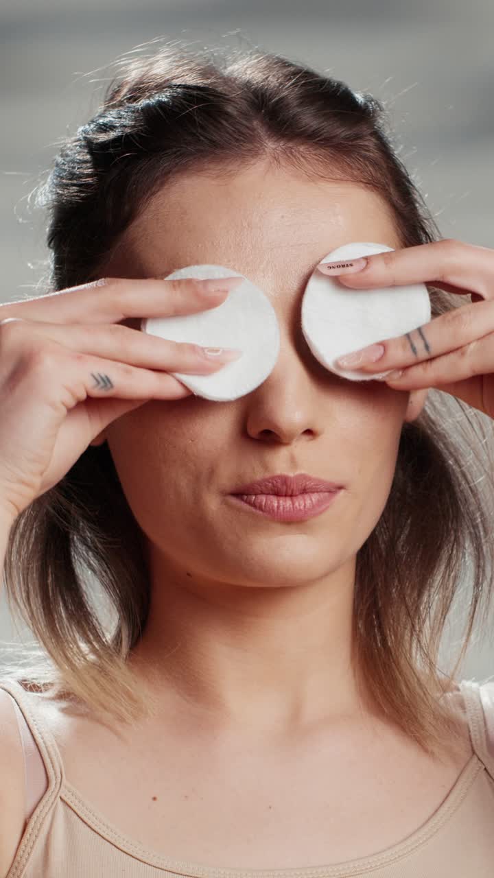 Vertical video: Cheerful beauty model playing with cotton pads on camera