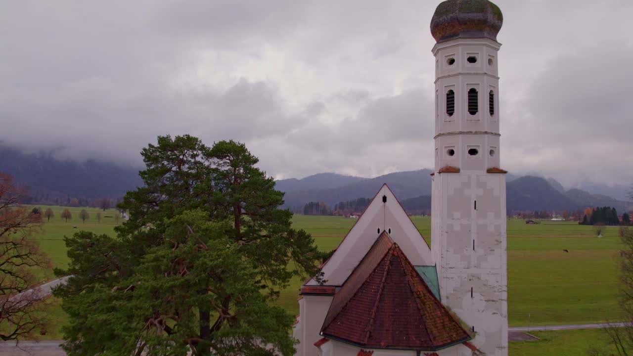Ilmakuva St. Colomanista pilvisen vuoristomaiseman taustalla, Baijeri, Saksa