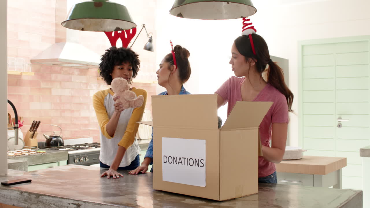 Women friends wearing festive headbands packing donations in kitchen for Christmas