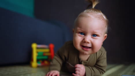 blue-eyed blond baby lies on the floor. smiling infant crawls to camera. close up.