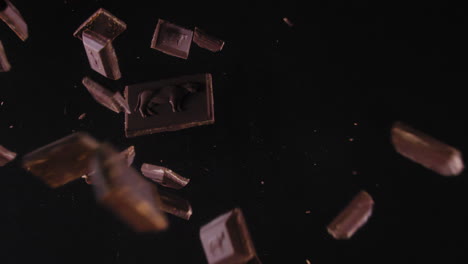 dark chocolate block falls on a black background, explodes and parts fly in the air - extreme slow motion top shot