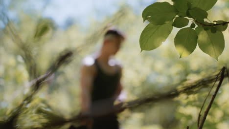 foggy view of tourist pulling off gloves while leaning against tree trunk, facing branch tip in blurred forest backdrop with dappled sunlight filtering through dense green leaves for serene forest