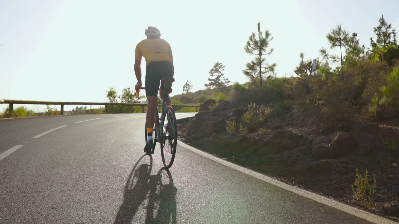 Against the serene backdrop of the morning, a man cycles on a road bike for outdoor exercise along an unoccupied road. The slow-motion perspective intensifies the thrill of extreme sports