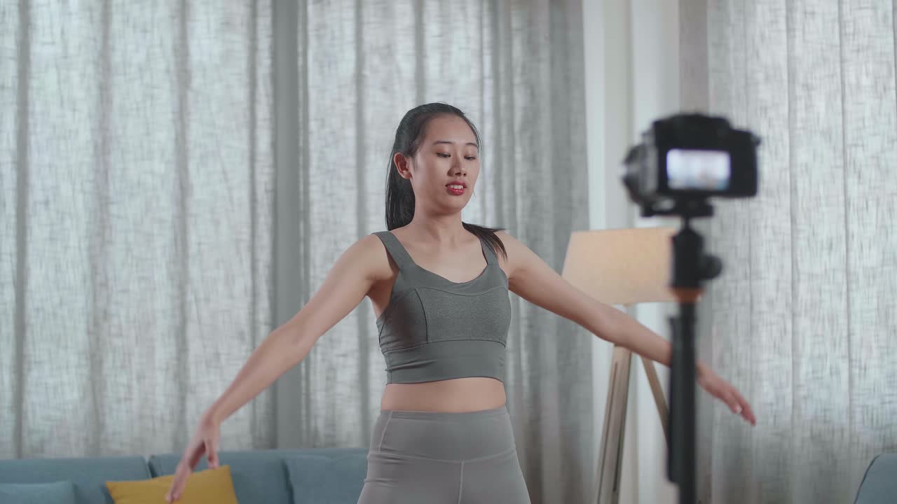 스포츠 옷을 입은 젊은 아시아 트레이너 여성이 카메라에 대화하고 집에서 가르치는 운동을 녹음하는 동안 스트레칭합니다.