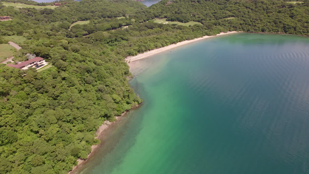 Aerial lowering over turquoise sea, sand shore and dense green rainforest coast in Nacascolo beach, Papagayo Peninsula, Costa Rica