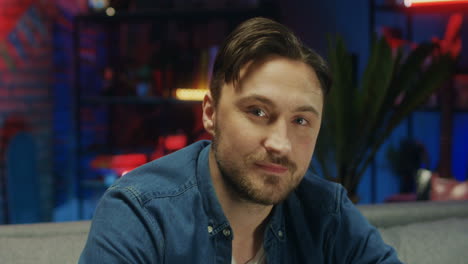 Portrait-Shot-Of-The-Handsome-Young-Guy-Smiling-Cheerfully-To-The-Camera-And-Drinking-Beer-In-The-Dark-Room