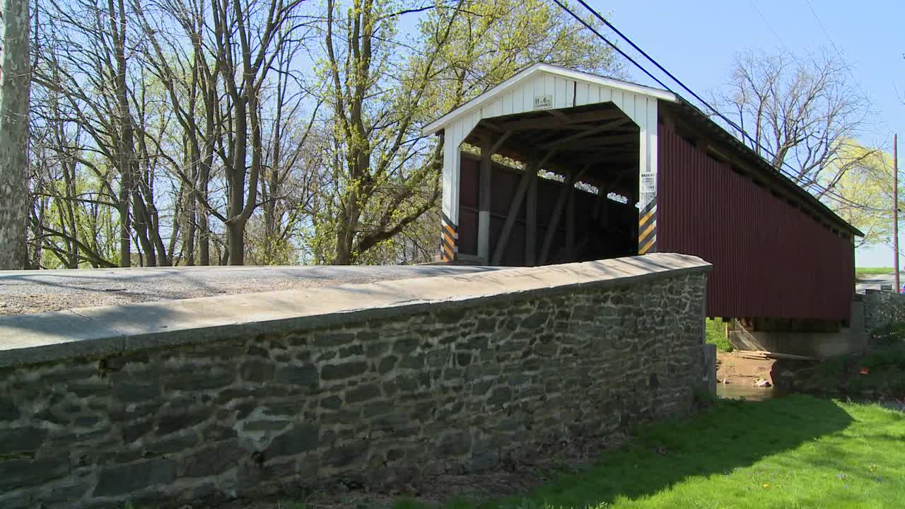 un carro amish de caballos y buggy pasa a través de un puente cubierto en la zona rural de lancaster, pensilvania.