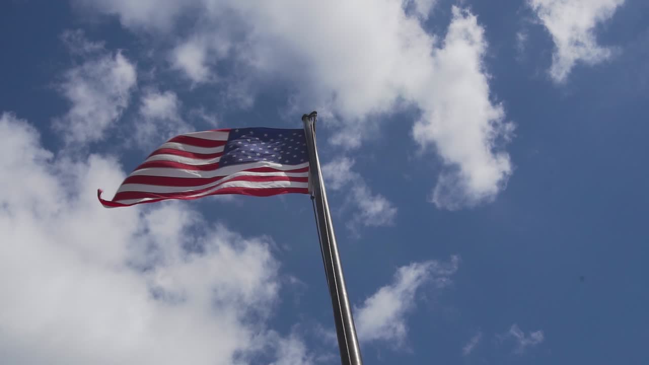 Bandiera americana che sventola sotto le nuvole sotto il sole estivo, angolazione bassa