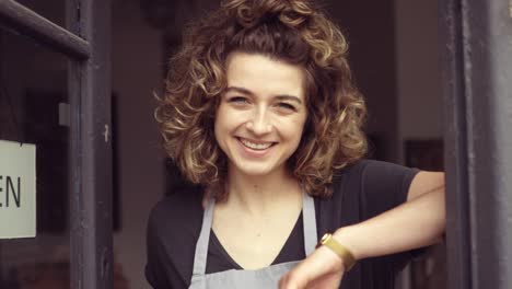 smiling young woman at the door of her shop welcoming customers