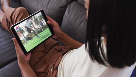 compuesto de una mujer sentada en casa en el sofá viendo un partido de hockey en la tableta