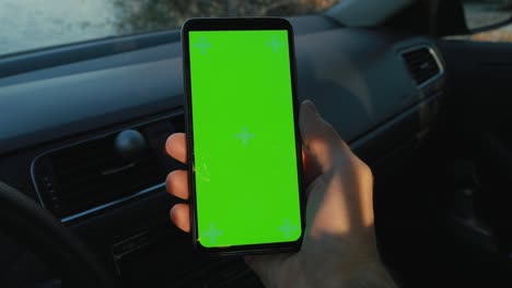 pov, hombre con la mano sosteniendo un teléfono inteligente con pantalla verde en un coche en el río