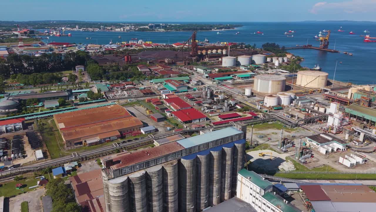 Aerial of Labuan's Rancha-Rancha Industrial Estate, Malaysia. The shot captures cement storage silos, a steel mill, and a sponge iron plant with many ships in the bay