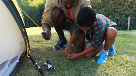 father teaching son how to tie a tent to the ground