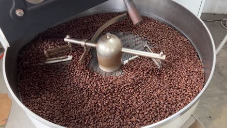 specialty coffee beans spinning on cooling and mixing tray to reduce the heat evenly after roasting, production warehouse factory shot of food and beverage industry, tilt down shot