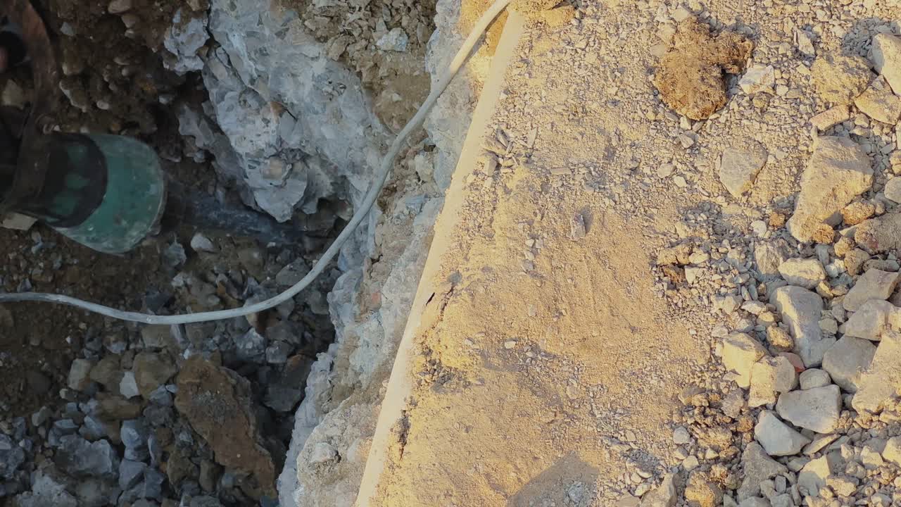 Top view of drilling machine working in dug trench with soil and rocks scattered around, rough terrain and equipment visible in an outdoor construction setting