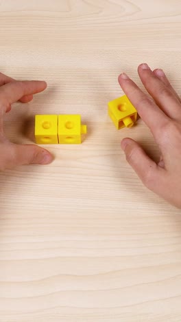 hands assembling yellow cubes on a wooden table