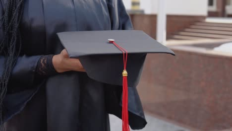 master's hat with a red tassel on the hand of a university graduate. close up view with an outdoor stairs onbackground