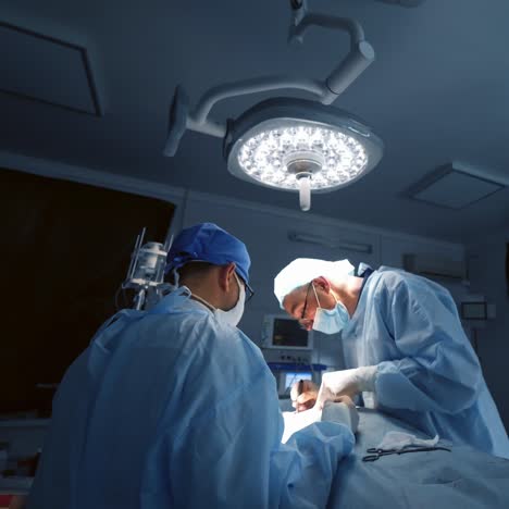 doctors during surgery in operating room. professional surgeons in medical uniform performing operation under the bright lamp in dark room at hospital.