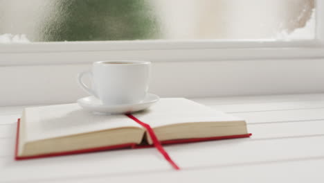 video of cup of hot coffee and book over frozen and snowy window