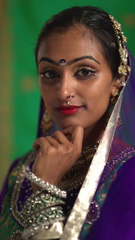 vertical video close up portrait of female kathak dancer performing dance wearing traditional indian dress and jewellery looking at camera