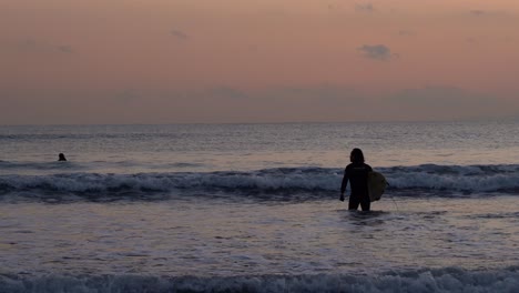 silhouette of a surfer walking into the beautiful sea with intense wave at dusk in japan - perfect for summer activities - wide shot