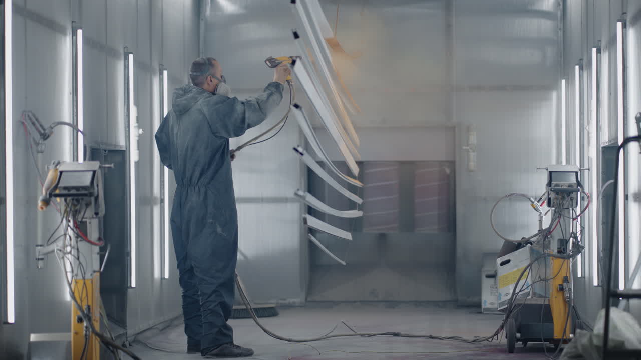 Un hombre con traje protector y mascarilla rocía pintura sobre las piezas. Taller de pintura de pequeña empresa. Taller para pintar piezas.