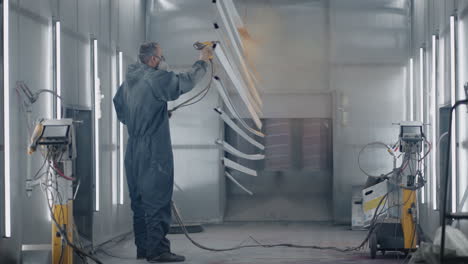 ein mann in schutzanzug und maske sprüht malerfarbe auf die teile. kleinbetriebsmalerei. werkstatt zum malen von teilen.