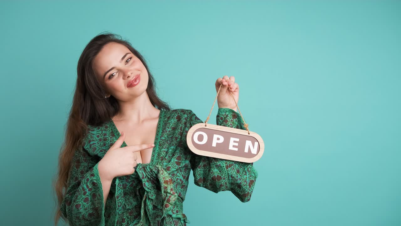 Smiling woman with open sign inviting in blue studio