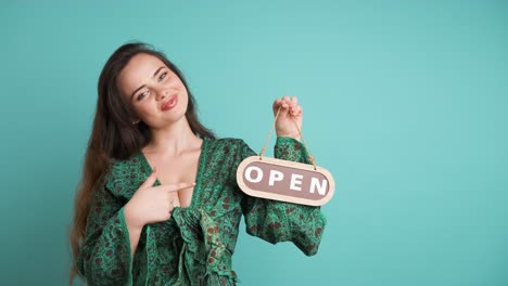smiling woman with open sign inviting in blue studio