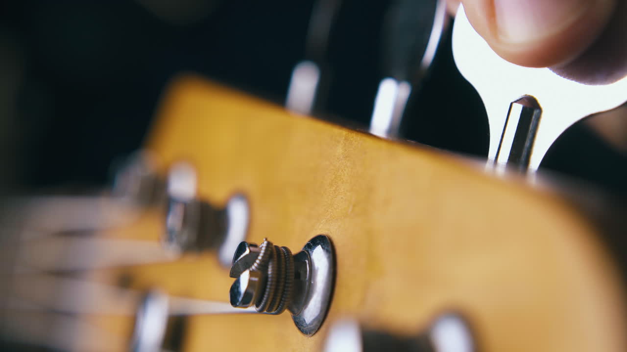 guitarist tunes second bass string with silver tuning key
