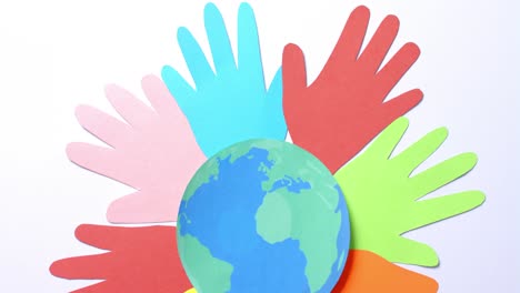 Close-up-of-hands-together-with-globe-made-of-colourful-paper-on-white-background-with-copy-space