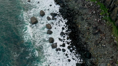Waves Splashing On Jagged Basalt Rocks Along Shoreline Of Isle Of Skye In Scotland, UK. aerial topdown, tilt-up shot