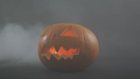 Smoke-effect-over-scary-face-carved-halloween-pumpkin-against-grey-background