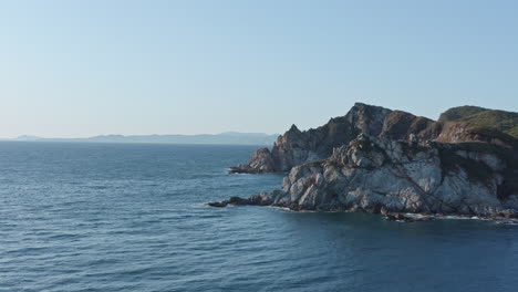 Bird's-eye-view-of-coastline-with-steep-cliffs,-underwater-rocks-on-the-sunset