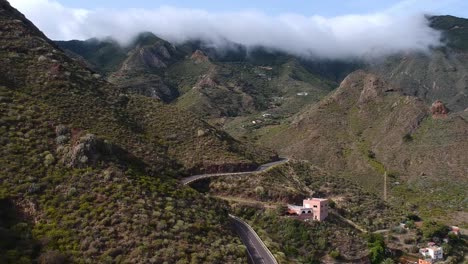 Clouds-rolling-over-mountain-tops-with-majestic-winding-road-in-foreground,-aerial-descend-view