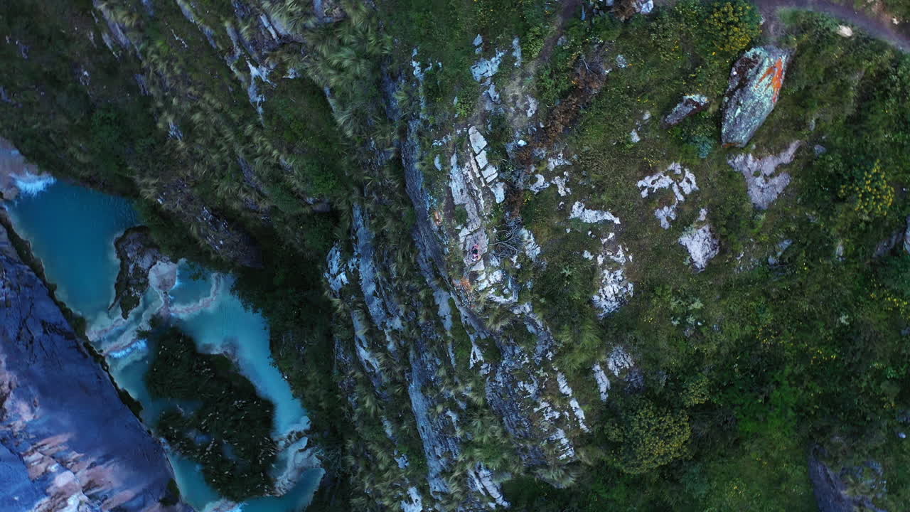 Amazing overhead drone shot of a person artist in brightly colored costumes dancing down the mountains around the purple water Millpu lake.