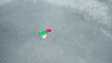 hombre poniendo una vara de pesca de hielo ligera y cebo en el lago congelado