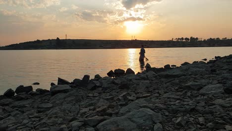 a fisherman wading in a calm lake during a spectacular sunset