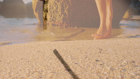 crucifix animation over person walking barefoot on sandy beach near water
