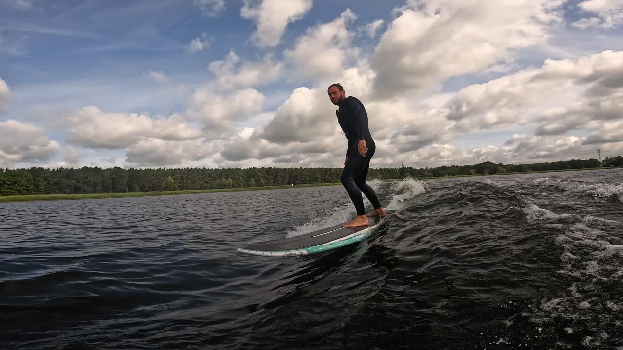 surfista en longboard surfeando olas en un lago con nubes en el cielo filmado con gopro 60fps