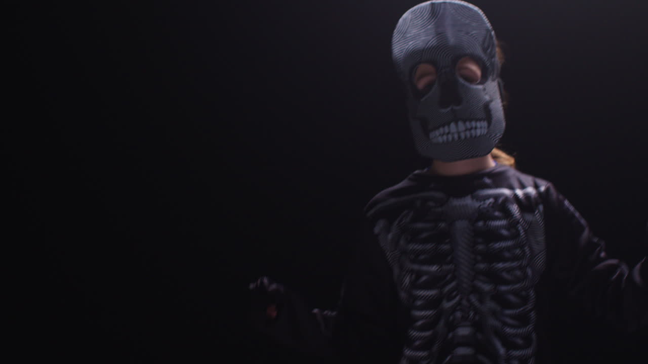 fotografía de estudio de un niño vestido con un disfraz de esqueleto haciendo un truco o un regalo en halloween bailando contra un fondo negro 3