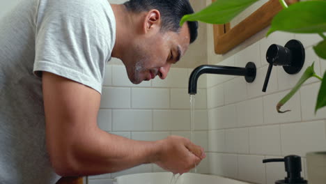 Man-washing-face-in-home-bathroom