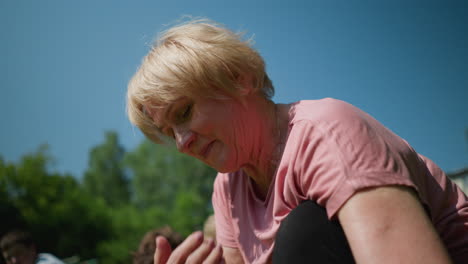 a close-up of a woman focused on her task, rubbing her neck with her right hand while outdoors, blurred figures are visible in the background